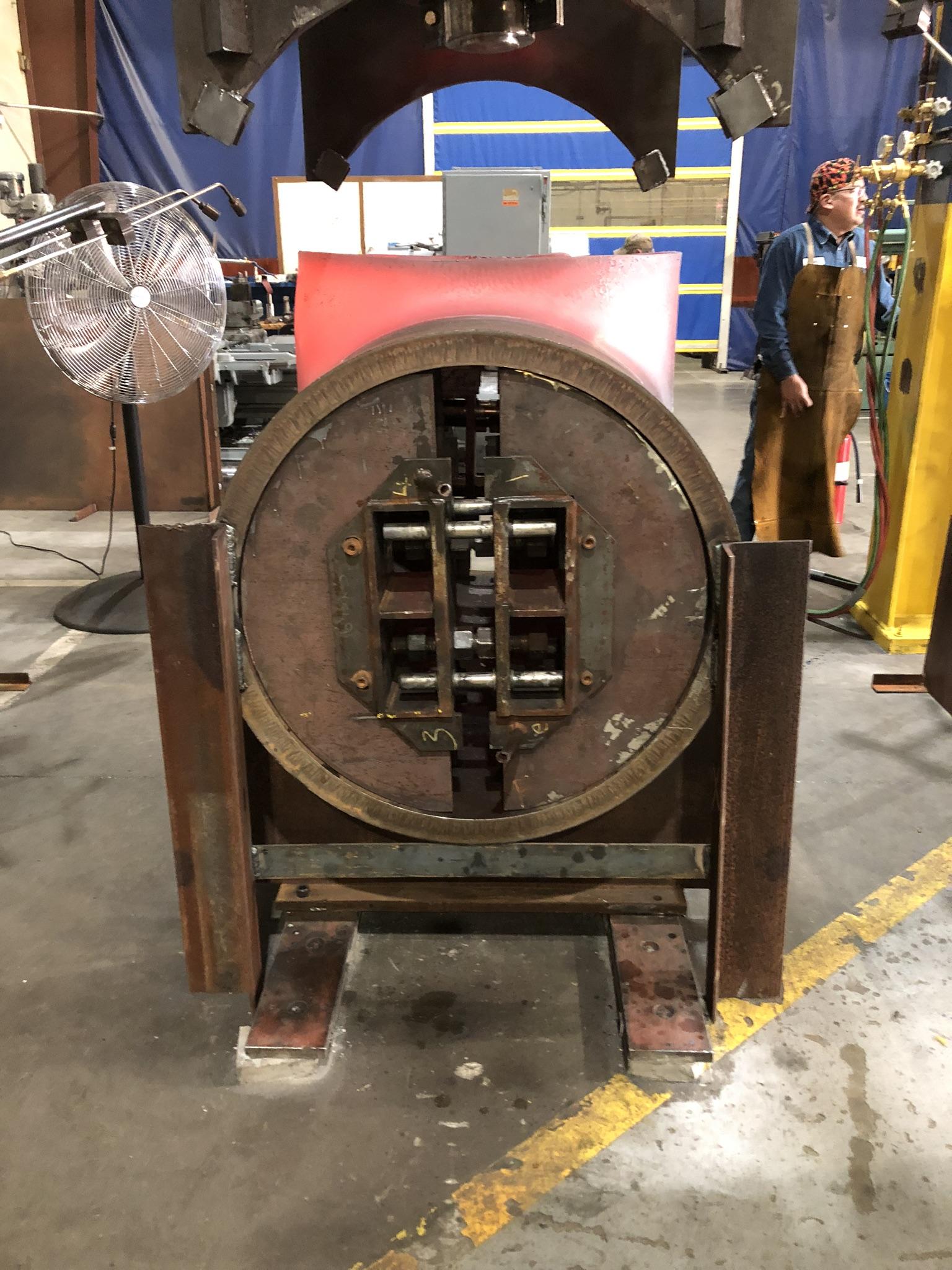 End-bell tooling clamped around a large pipe fitting on the press